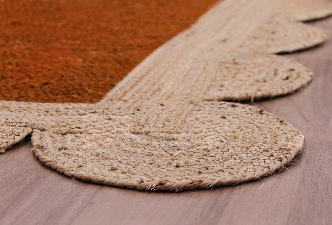 A close-up of a natural jute or seagrass rug with a scalloped edge, laid over a terracotta-colored rug on a light wood floor.