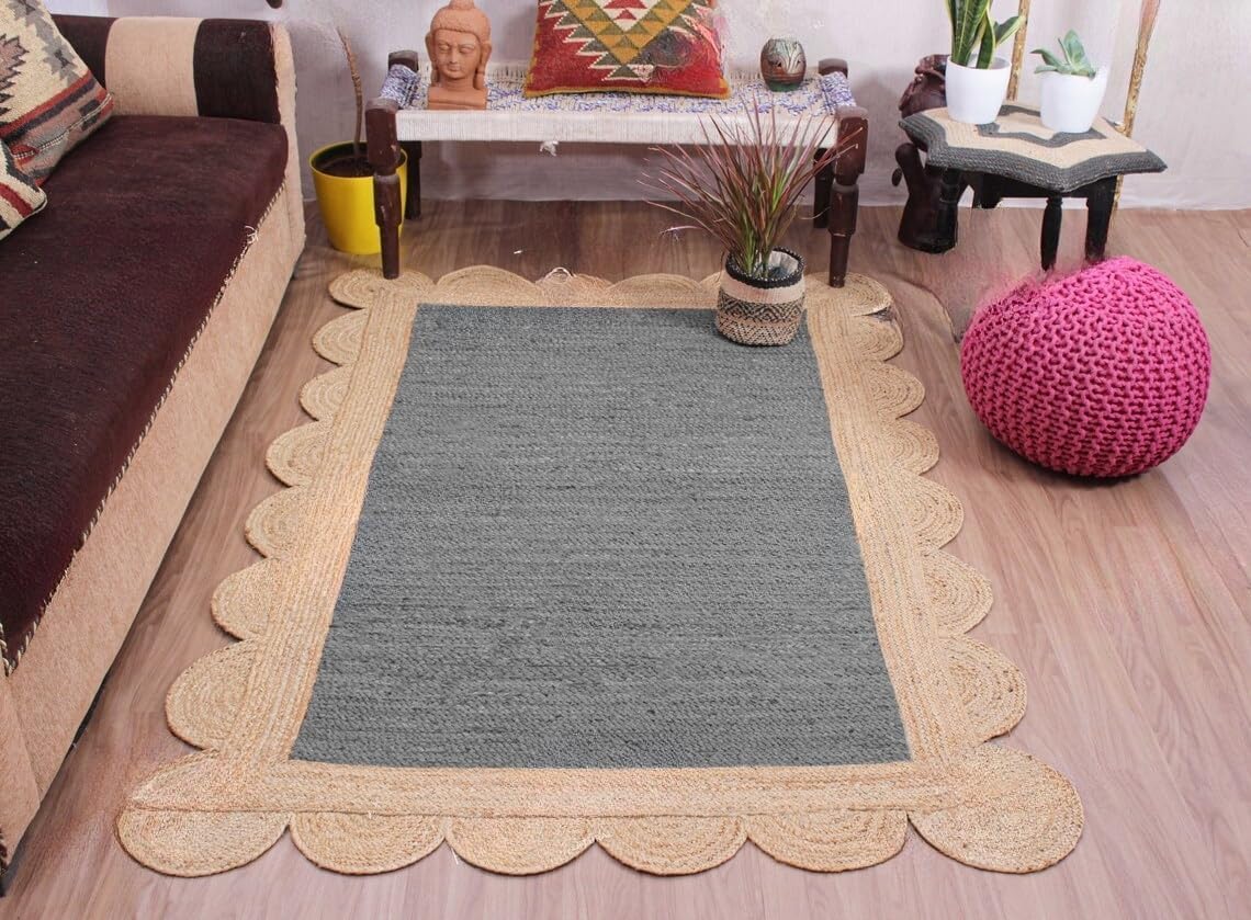 A rectangular gray woven rug with a scalloped natural jute border, displayed on a light wood floor in a styled living room setting.