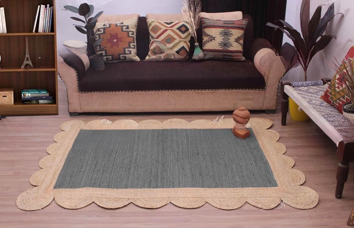 A rectangular area rug with a scalloped natural jute border and a textured gray-green center, styled in a living room setting in front of a brown sofa.
