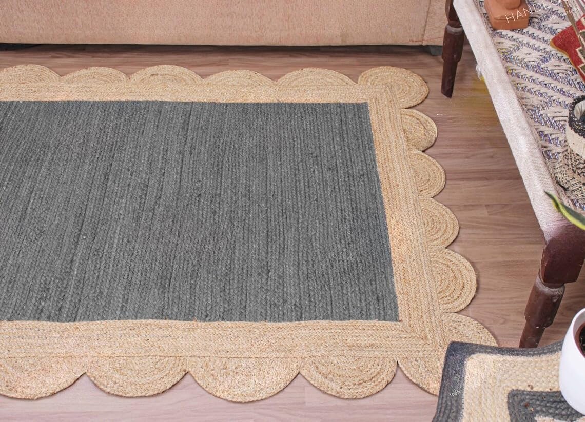A rectangular woven runner rug with a scalloped braided border, shown on a wood floor in a home setting next to a sofa and table.