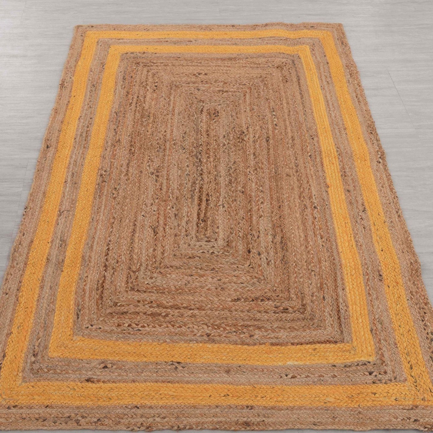 Brown braided rug with yellow border on a gray floor