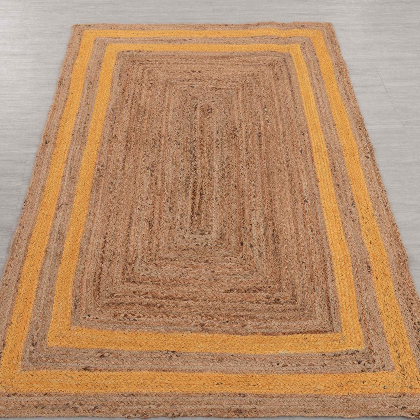 Brown braided rug with yellow border on a gray floor