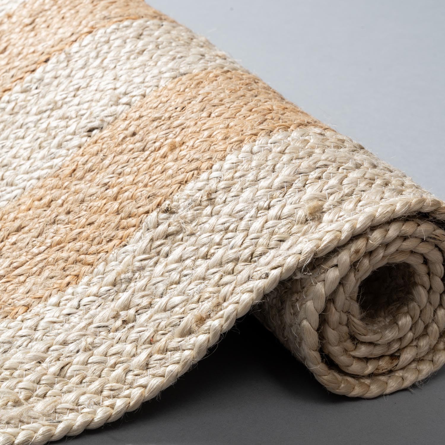 Rolled jute rug with natural beige and white pattern on a gray background