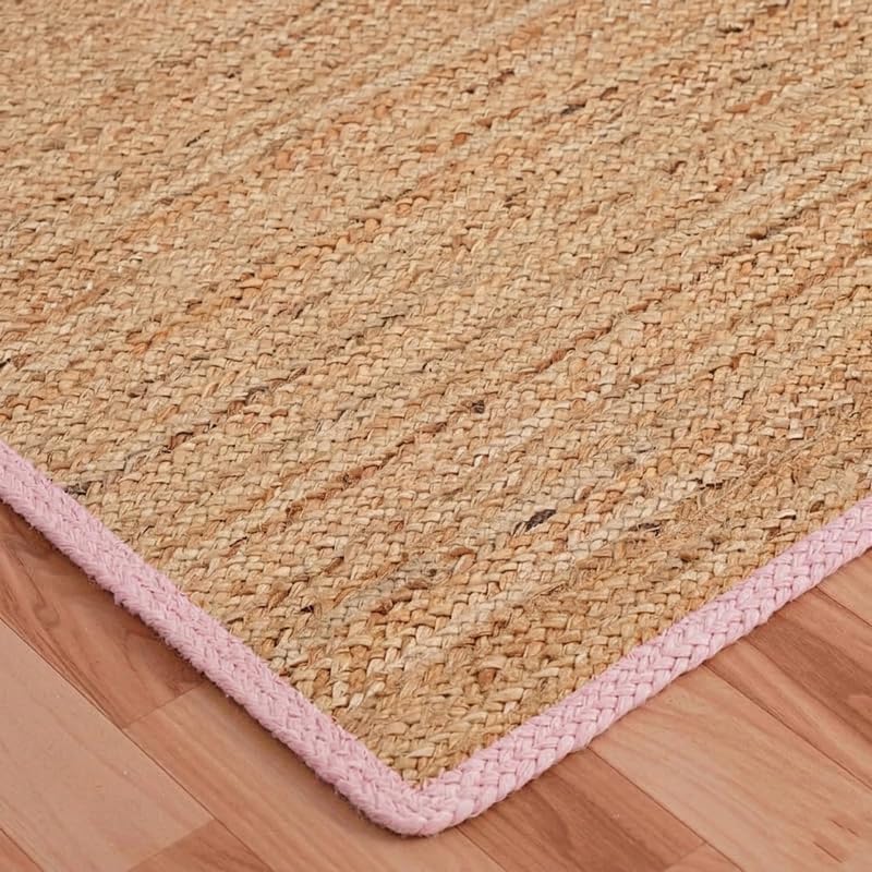 Natural Jute Area Rug with pink braided border on indoor wooden floor corner