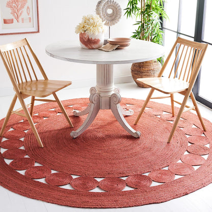 Round coral woven area rug with a decorative pattern under a wooden dining table and chairs.