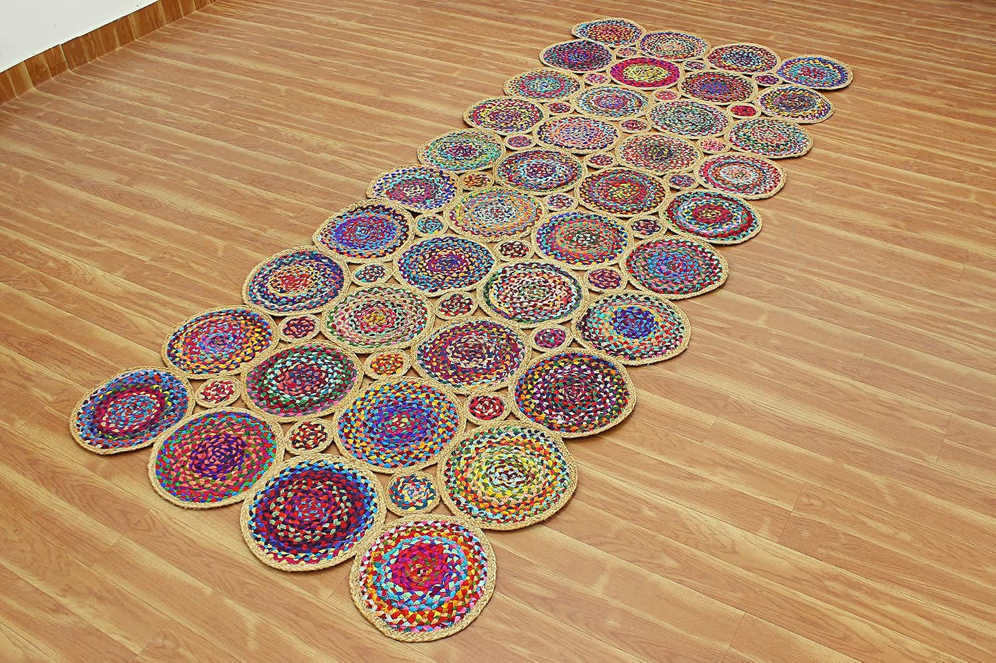 A long, narrow arrangement of colorful circular woven rugs laid out diagonally on a light wood floor.