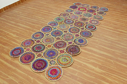 A long, narrow arrangement of colorful circular woven rugs laid out diagonally on a light wood floor.
