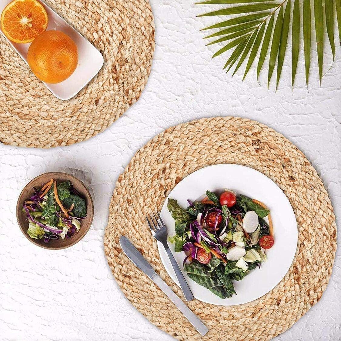Colorful salad on a white plate with a woven placemat, oranges, and a small bowl of greens on a textured surface.