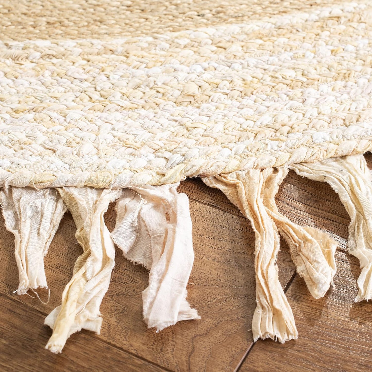 Close-up of a woven beige rug with tassels on a wooden floor.