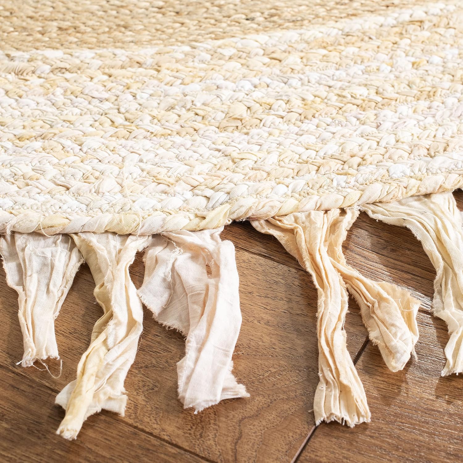 Close-up of a woven beige rug with tassels on a wooden floor.