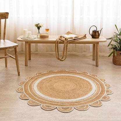 A round braided jute rug with a scalloped edge, styled in a bright, modern room on a light wood floor in front of a low wooden table.