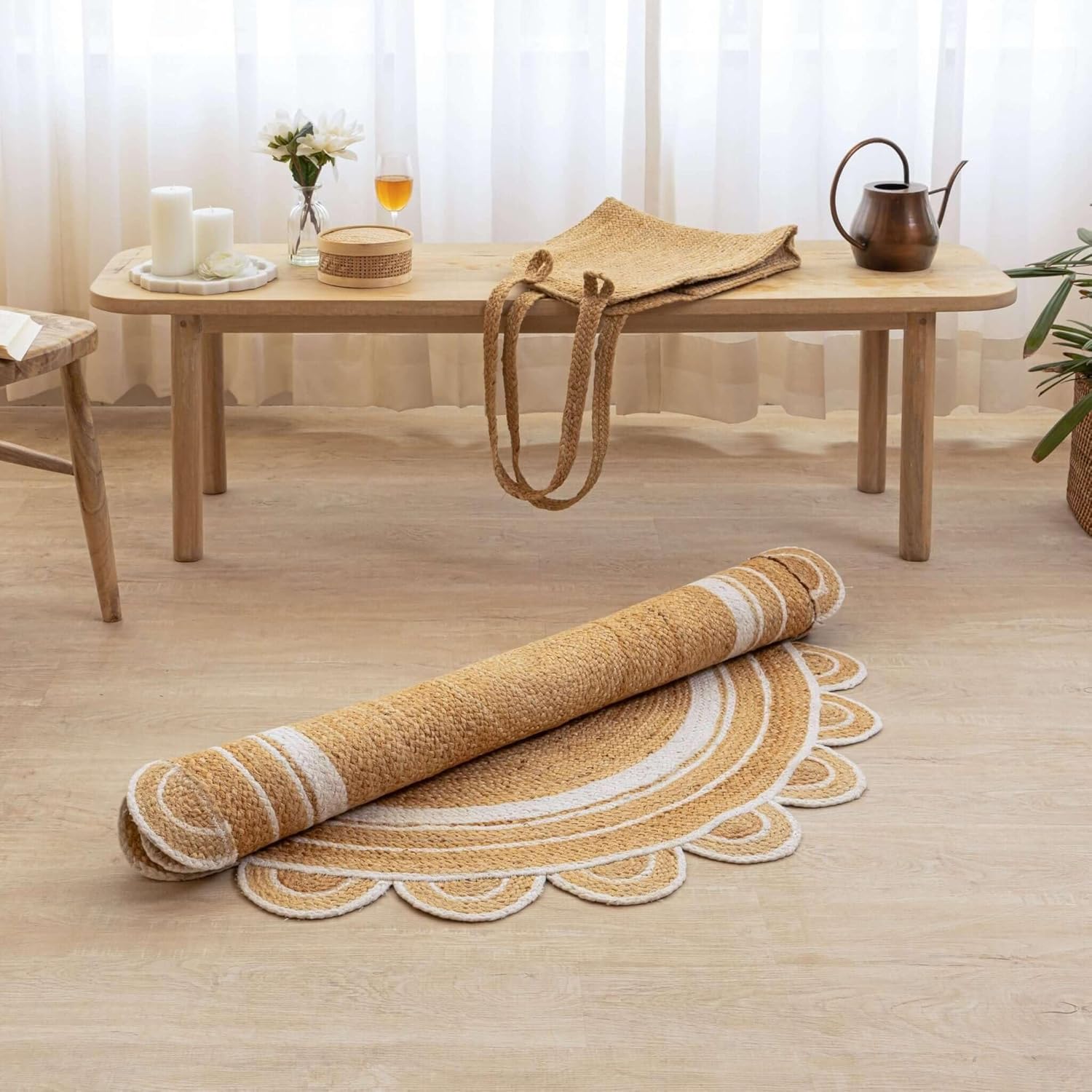 A round jute rug with a scalloped edge, shown partially unrolled on a light wood floor in a styled room setting with a wooden bench and table in the background.