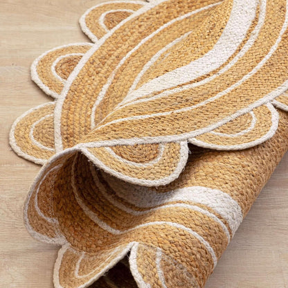 A close-up of a rolled woven rug with a scalloped leaf-like pattern in natural tan and off-white, shown on a light wood floor.