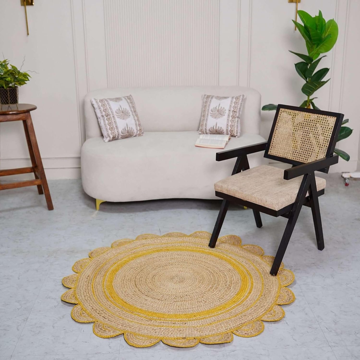 A round braided jute area rug with a scalloped edge and concentric yellow stripes, styled in a modern living room setting next to a white sofa and a black wooden chair.