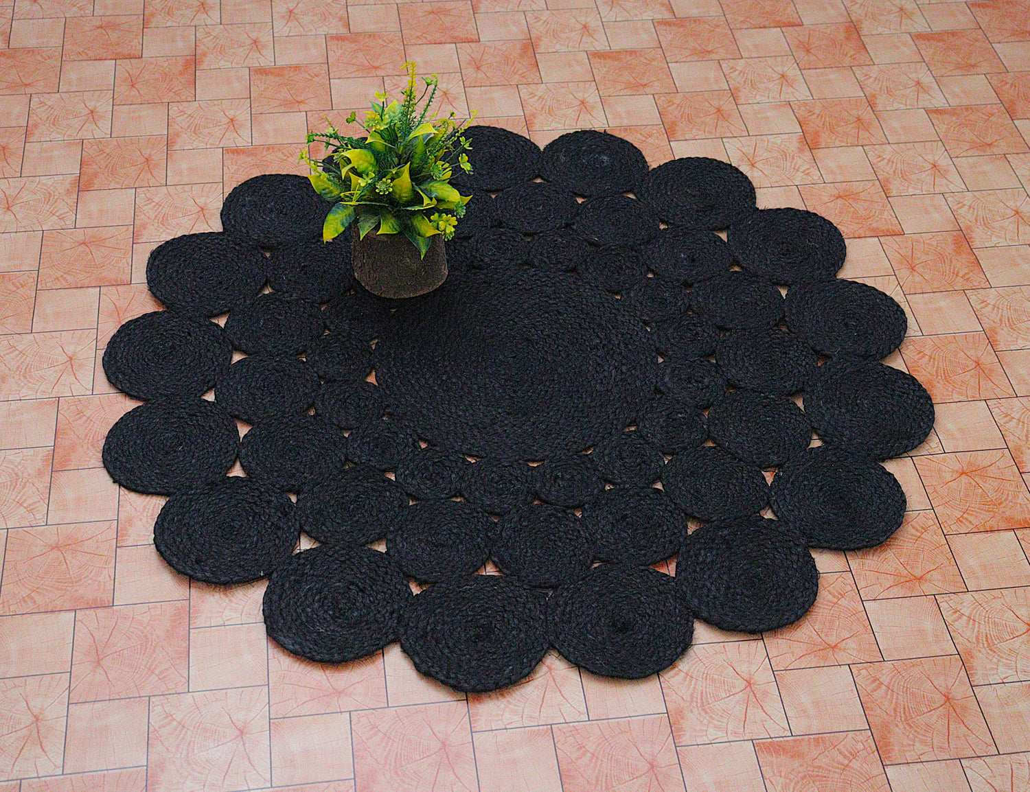 Black crocheted doily on a tiled floor with a small plant in the center.