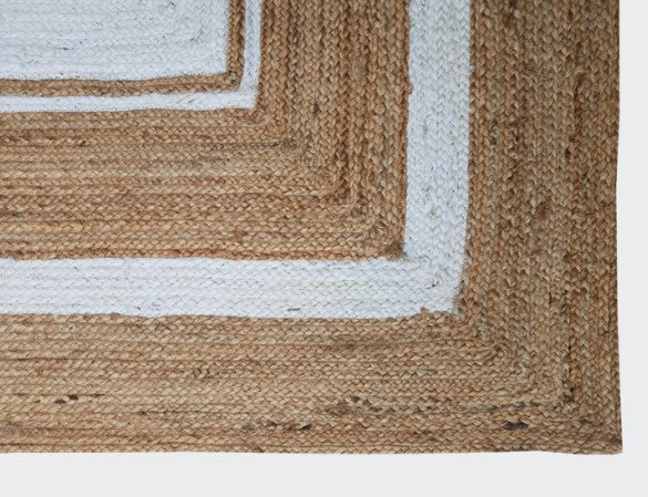 Close-up of a woven jute rug with a white border on a plain background
