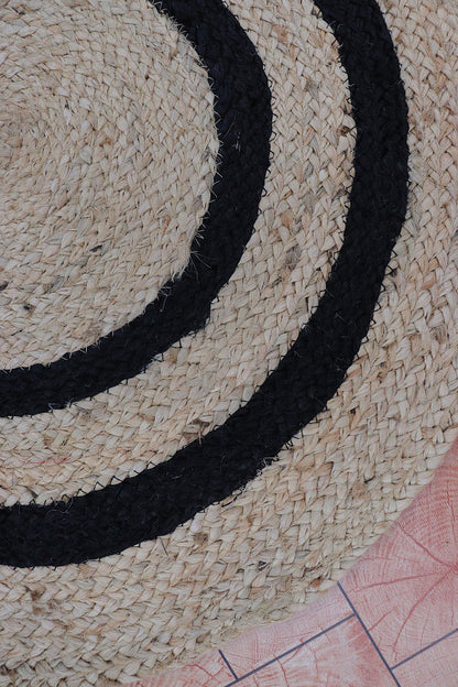 Close-up of a woven mat with black circular pattern on a textured surface.