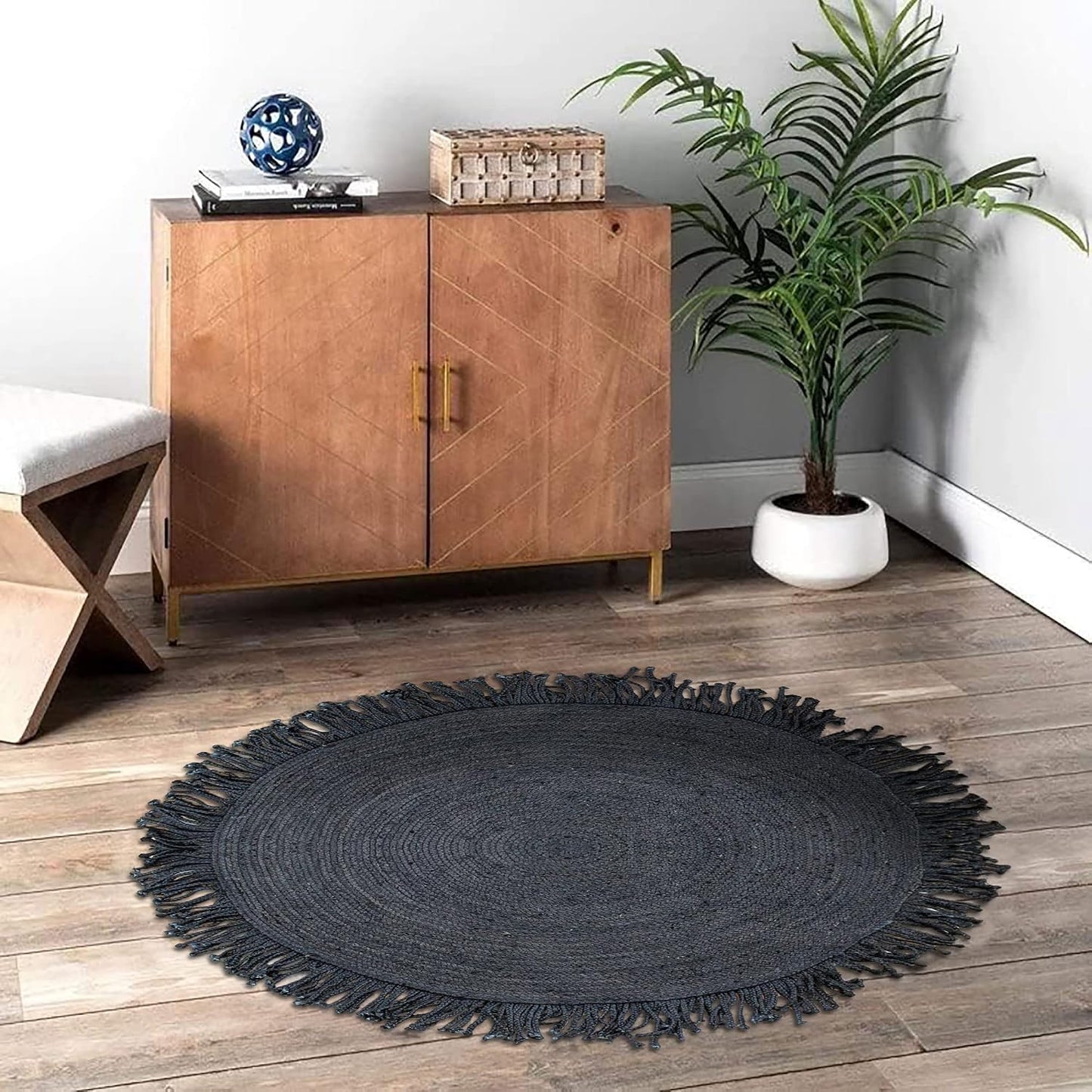 Round black rug on a wooden floor with a wooden cabinet and plant in the background.