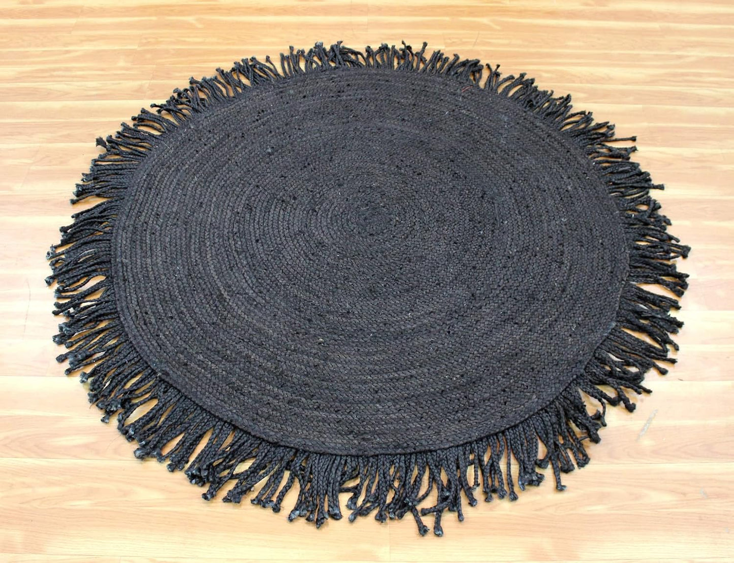 A round black woven placemat with fringed edges, laid flat on a light wood floor.