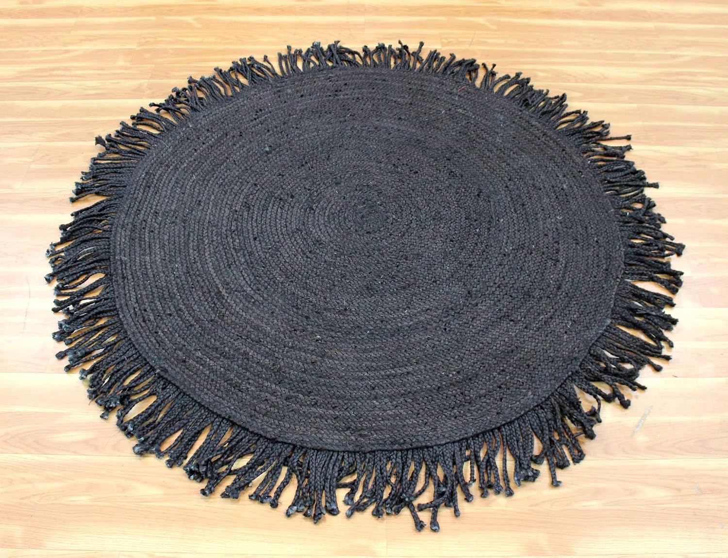 A round black woven placemat with fringed edges, laid flat on a light wood floor.