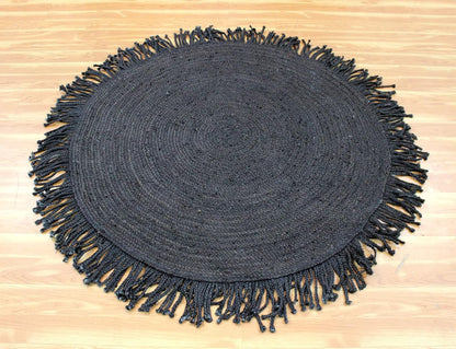 A round black woven placemat with fringed edges, laid flat on a light wood floor.