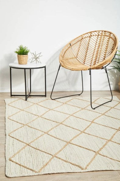 Woven chair on a geometric patterned rug with a small table and plant in the background.