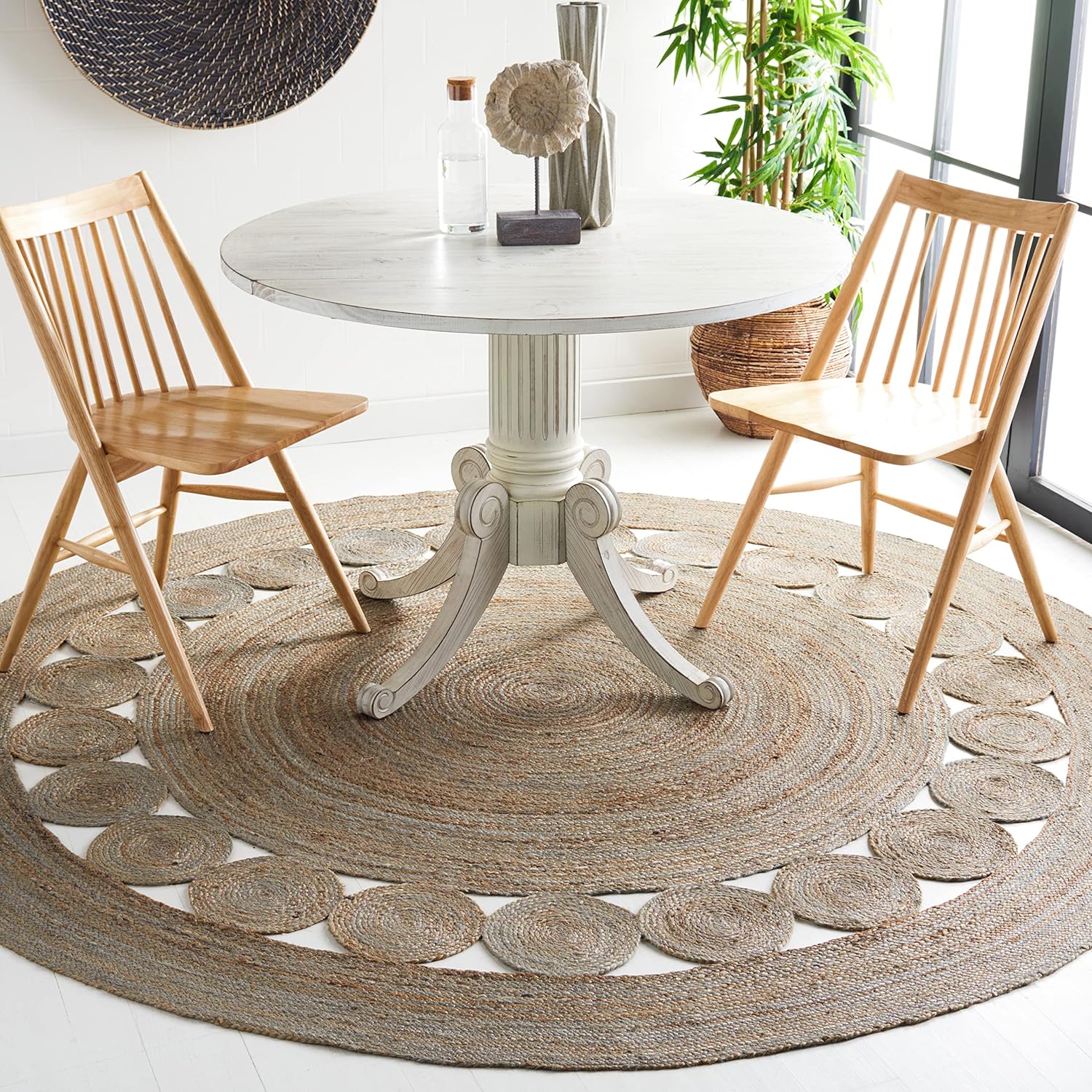 Rustic round dining table with two wooden chairs on a woven jute rug, showcasing natural textures.