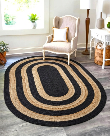 Handmade black and natural oval jute rug placed in a modern living room with a durable handwoven braided design.