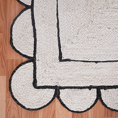 White braided rug with black scalloped edge on a wooden floor