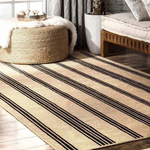 Striped beige and black rug in a room with a woven ottoman and wooden bench.