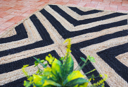 Geometric patterned doormat with a plant in the foreground on a brick pavement.